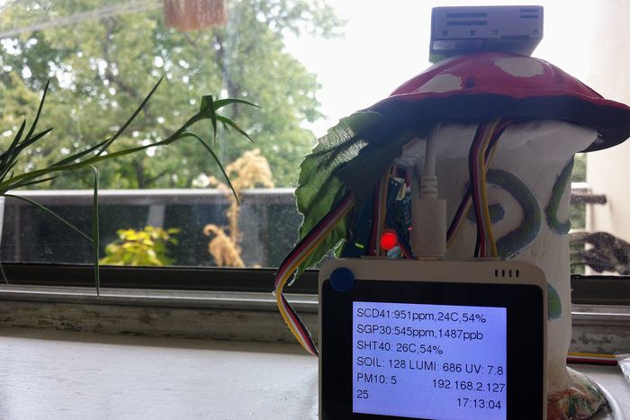 A sensor build hidden inside a painted toadstool ornament on a windowsill, its screen listing readings from several sensors at once.