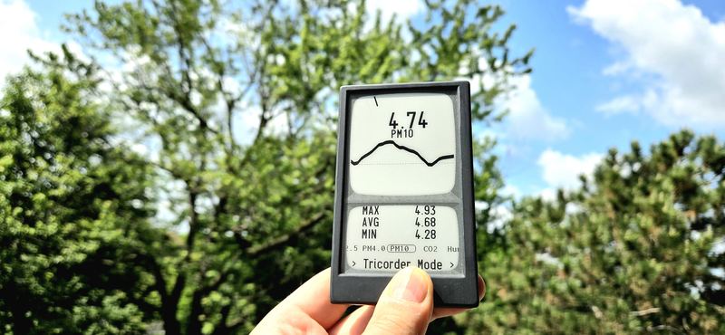 A Canary held up against trees and blue sky in Tricorder mode, showing 4.74 PM10 with max, average and minimum.
