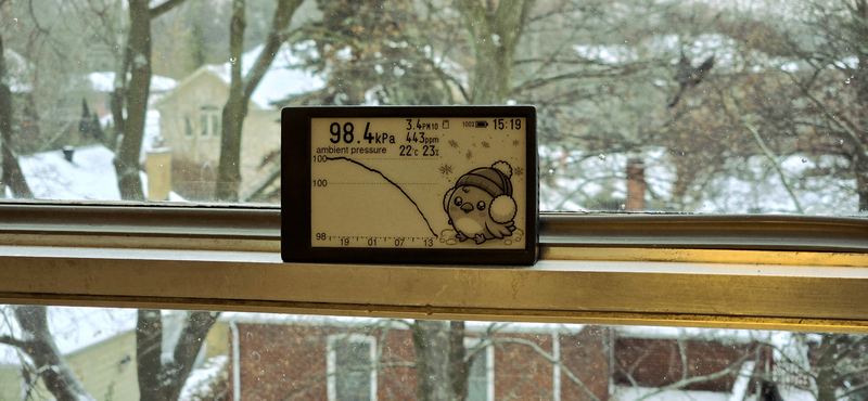 A Canary on a windowsill above a snowy street, showing ambient pressure dropping steeply.